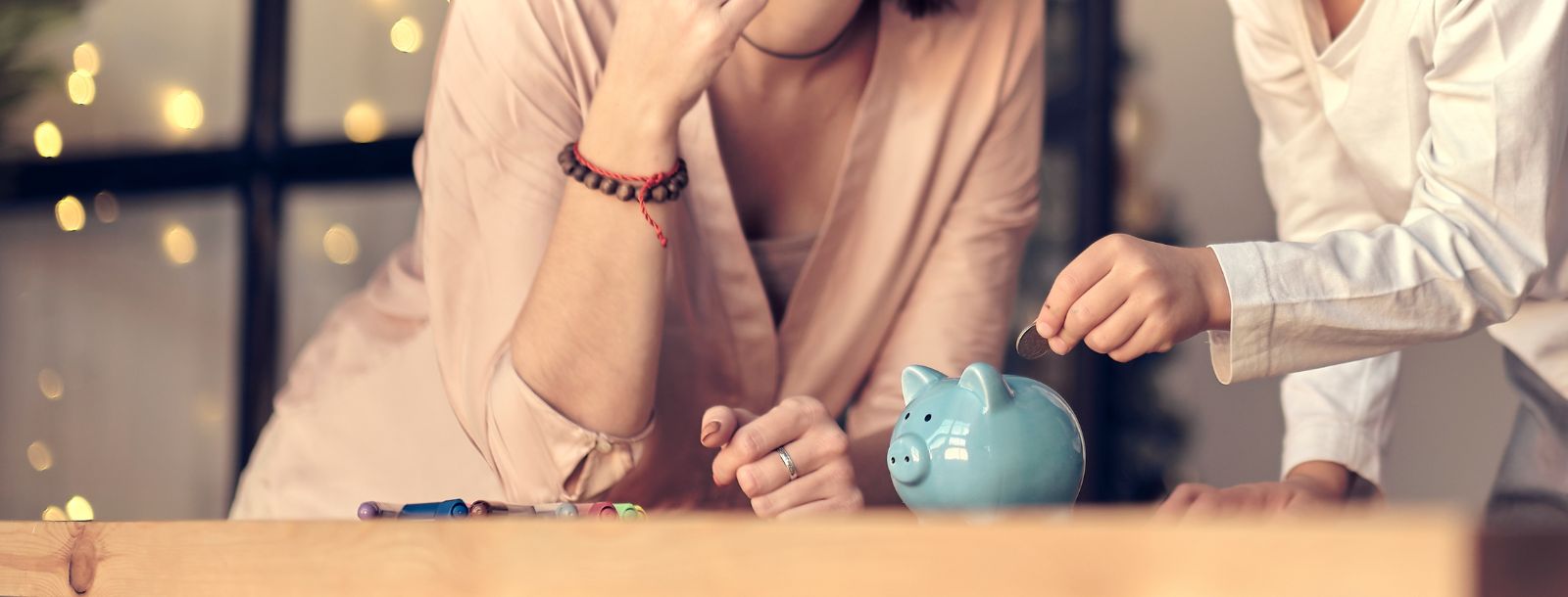 Two people putting money into a piggy bank that is sitting on a counter top.